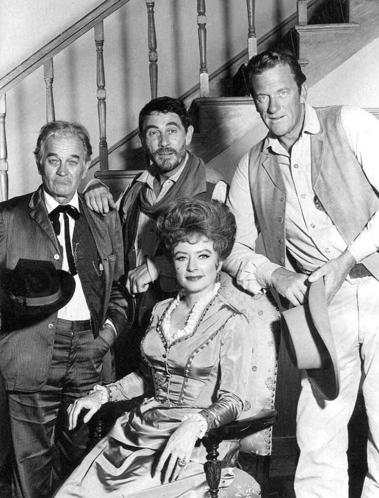 Main cast photo from the television program Gunsmoke in 1967. Standing, from right: James Arness as Marshall Matt Dillon, Ken Curtis as Festus Hagen, and Milburn Stone as "Doc" Adams. Seated: Amanda Blake as "Miss Kitty" Russell.